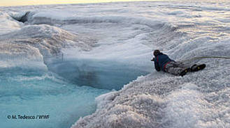 Researchers on safety ropes edge towards a cascade pouring into a newly opened crack on the Greenland ice sheet