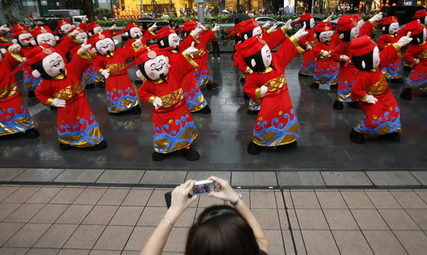 A bystander takes pictures as performers dressed as Chinese Fortune Gods dance during a flash mob in the Orchard Road shopping district in Singapore Jan 29, 2011. [China Daily/Agencies]