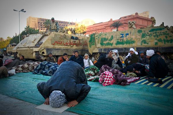 A demonstrator prays beside an armoured vehicle at Tahrir Square in Cairo, capital of Egypt, Feb. 8, 2011. Demonstrations demanding resign of President Hosni Mubarak continued, though the new government approved 15-percent pay raise for government employees. 