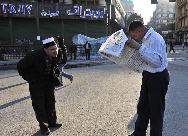 Two men read news papers at Tahrir Square in Cairo, capital of Egypt, Feb. 8, 2011. Demonstrations demanding resign of President Hosni Mubarak continued, though the new government approved 15-percent pay raise for government employees. 