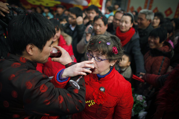 Rebecca Kanthor (R) and Liu Jian (L) drink red wine as part of their traditional Chinese wedding in Dong'an at the central province of Henan, February 9, 2011. [China Daily/Agencies]