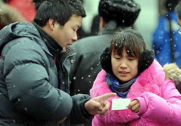 Two passengers check a train ticket while waiting for getting into Zhengzhou Railway Station amid heavy snow during China&apos;s Spring Festival travel rush in Zhengzhou, capital of central China&apos;s Henan Province, Feb. 9, 2011. China&apos;s central area witnessed the first snow of this year on Wednesday. [Xinhua]