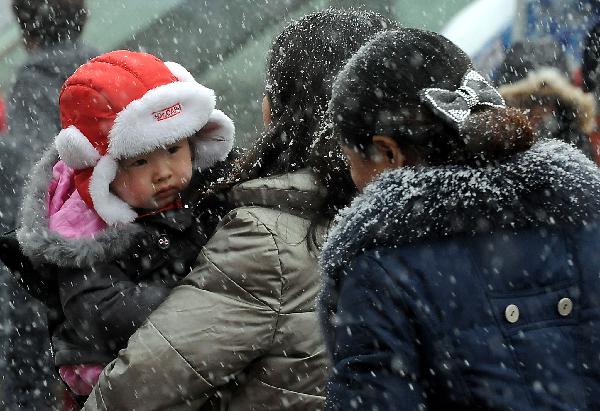 A child carried by her mother gets into Zhengzhou Railway Station amid heavy snow during China&apos;s Spring Festival travel rush in Zhengzhou, capital of central China&apos;s Henan Province, Feb. 9, 2011. China&apos;s central area witnessed the first snow of this year on Wednesday. [Xinhua] 