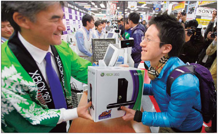 Takashi Sensui, general manager of Microsoft Corp's home and entertainment division, hands a Kinect for Xbox 360 to a customer at an electronics chain in Tokyo. Sales of the online gaming product have proved to be very successful in Asia. [China Daily]