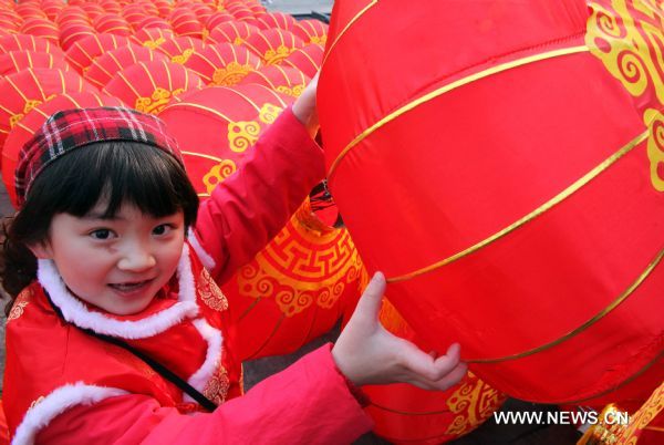 A girl poses for photos with a red lantern, which is about to be hung up, at Qianmen Avenue in Beijing, capital of China, Feb. 15, 2011. A carnival began at the avenue Tuesday, including lantern show, dragon dances, Peking Opera performances, to celebrate the upcoming Lantern Festival which falls on Feb. 17, 2011. (Xinhua/Chen Xiaogen) (ly) 