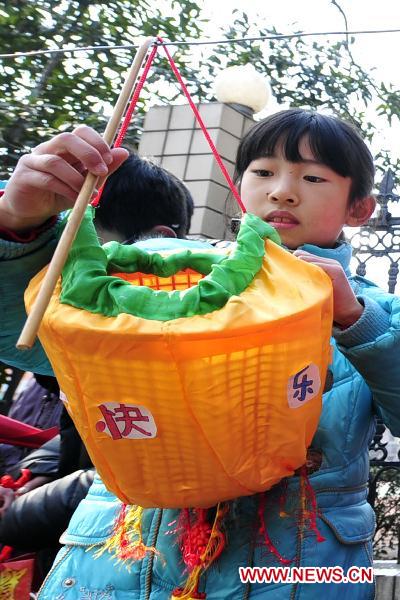 A pupil hangs a lantern made by herself with wasted materials at the gate of Qiushi Primary School in Hangzhou, capital of east China's Zhejiang Province, Feb. 15, 2011. A lantern carnival in the theme of low carbon will be held in the school to celebrate the Lantern Festival that falls on Feb. 17, 2011. Some 800 low carbon lanterns have already been submitted up to now. [Li Zhong/Xinhua]