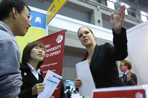 A worker with an overseas education institution introduces her school to two Chinese students at an international education fair in Beijing on Oct 16, 2010.