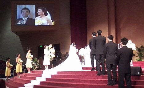 Skype wedding: Bride Helen Oh stands alone at the altar as her husband-to-be Samuel Kim watches her from his isolation ward on the jumbo-sized screen.