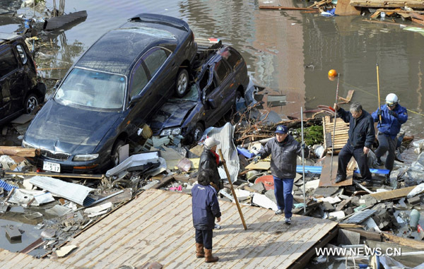 Earthquake and tsunami victims make their way past debris and water in Miyagi Prefecture, northeastern Japan March 12, 2011. Japan confronted devastation along its northeastern coast on Saturday, with fires raging and parts of some cities under water after a massive earthquake and tsunami that likely killed at least 1,000 people. 