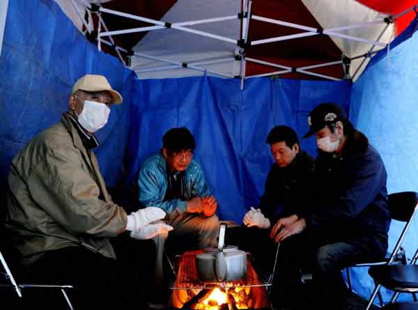 People warm themselves by a heater at an evacuation centre in Rikuzentakata, Iwate Prefecture in northeastern Japan March 12, 2011. [Xinhua]