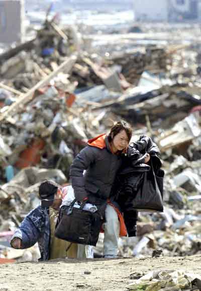 A woman carries her belongings away from her tsunami-stricken home in Rikuzentakata, Iwate Prefecture in northeastern Japan March 12, 2011. [Xinhua] 