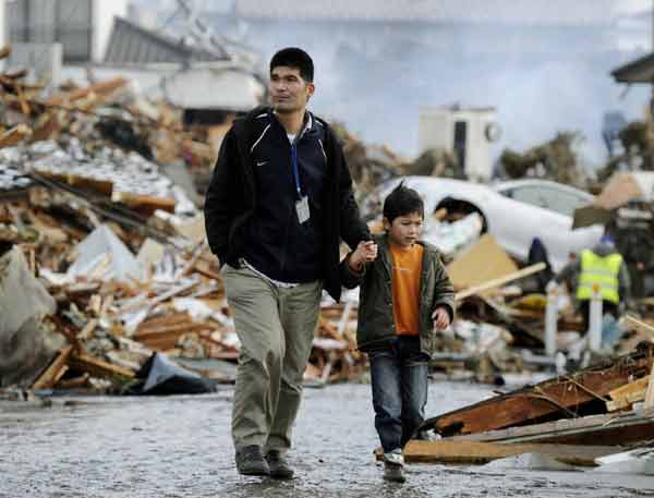 A man and boy walk between houses destroyed by a tsunami and earthquake in Sendai, northeastern Japan March 12, 2011. [Xinhua]