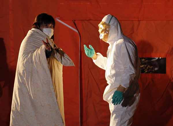 Official in protective gear talks to a woman who is from the evacuation area near the Fukushima Daini nuclear plant in Koriyama March 13, 2011. [Xinhua]