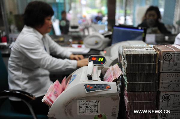 A bank staff member has a banknote counter checking RMB cash in Qionghai City, south China's Hainan Province, March 16, 2011. [Xinhua] 