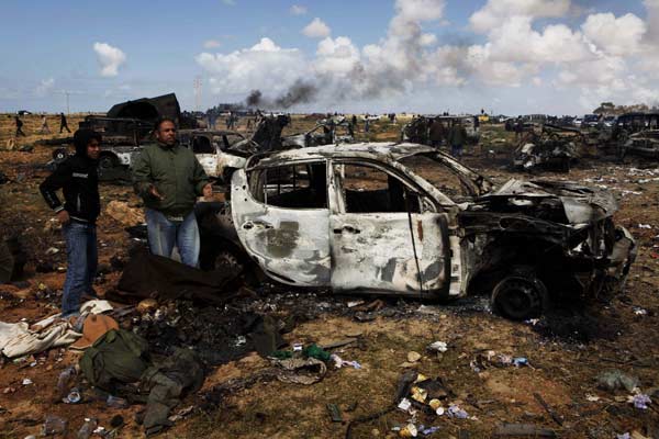 People stand near bodies that are under a blanket, of Muammar Gaddafi supporters killed in what residents said was a French airstrike early on Sunday morning on the southern outskirts of Benghazi in northeastern Libya, March 20, 2011.