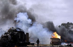 A rebel fighter looks at burning vehicles belonging to forces loyal to Libyan leader Muammar Gaddafi after an air strike by coalition forces, along a road between Benghazi and Ajdabiyah March 20, 2011. [Xinhua]