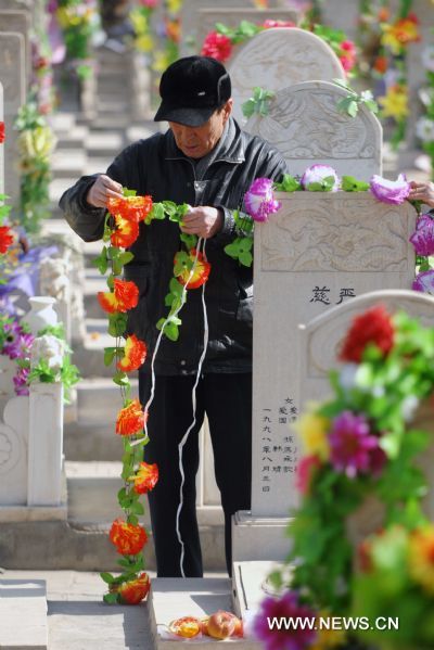 A citizen offers silk flowers as sacrifice to the deceased in a cemetery in Yinchuan, capital of northwest China's Ningxia Hui Autonomous Region, March 29, 2011. As the Tomb Sweeping Day approaches, which falls on April 5 this year, many people in Yinchuan chose to pay respect to the tombs of their deceased beloved ones with flowers instead of burning joss paper and setting off firecrackers which are harmful to environment. [Peng Zhaozhi/Xinhua]