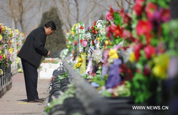 A citizen offers flowers as sacrifice to the deceased in a cemetery in Yinchuan, capital of northwest China's Ningxia Hui Autonomous Region, March 29, 2011. As the Tomb Sweeping Day approaches, which falls on April 5 this year, many people in Yinchuan chose to pay respect to the tombs of their deceased beloved ones with flowers instead of burning joss paper and setting off firecrackers which are harmful to environment. [Peng Zhaozhi/Xinhua]