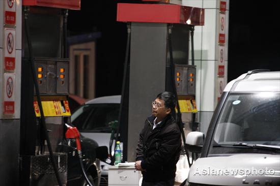 A man looks at a notice board as the tank of his car is filled at a gas station in Dalian, Northeast China's Liaoning province, April 6, 2011. [Photo/Asianewsphoto]