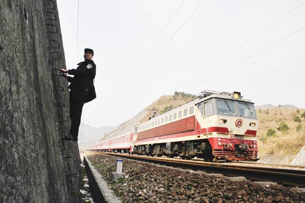 A police officer for the Tongren Railway Station, Guizhou province, checks safety along the line as a passenger train passes in February. [Photo/China Daily]