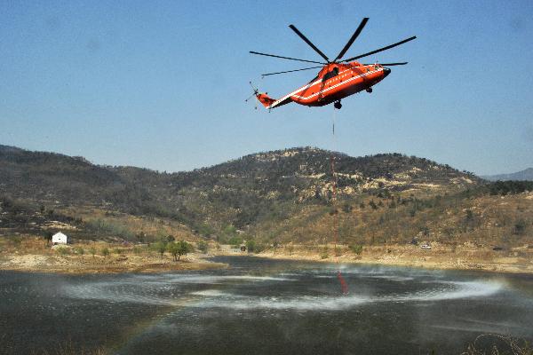 A firefighting helicopter loads water near the site of a mountain fire in east China&apos;s Shandong Province, April 19, 2011. A Mi-26 helicopter was sent to help extinguish a mountain fire that broke out here Monday morning. The fire was put off Tuesday before it reached the tourist site of Mount Tai. [Xinhua] 