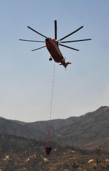 A firefighting helicopter trails a load of water to the site of a mountain fire in east China&apos;s Shandong Province, April 19, 2011. A Mi-26 helicopter was sent to help extinguish a mountain fire that broke out here Monday morning. The fire was put off Tuesday before it reached the tourist site of Mount Tai. 