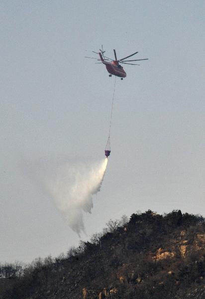 A firefighting helicopter releases water over flames at the site of a mountain fire in east China&apos;s Shandong Province, April 19, 2011. A Mi-26 helicopter was sent to help extinguish a mountain fire that broke out here Monday morning. The fire was put off Tuesday before it reached the tourist site of Mount Tai.