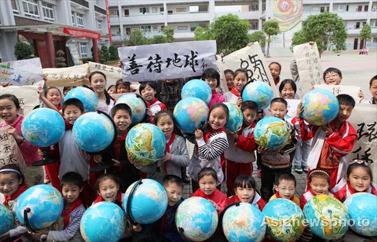 Students show globes and their calligraphy, urging people to protect the earth, for the upcoming Earth Day, April 22, at an elementary school in Southwest China&apos;s Chongqing municipality, April 19, 2011. 