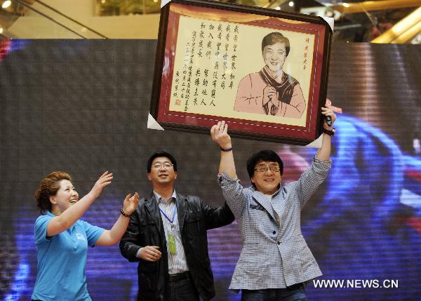 Movie star Jackie Chan (R) raises his portrait, a gift presented by local aid fundation for the youth and children's growth, at the opening ceremony of the cinema named after him in Shenyang, capital of northeast China's Liaoning Province, April 20, 2011. [Wang Jiang/Xinhua]