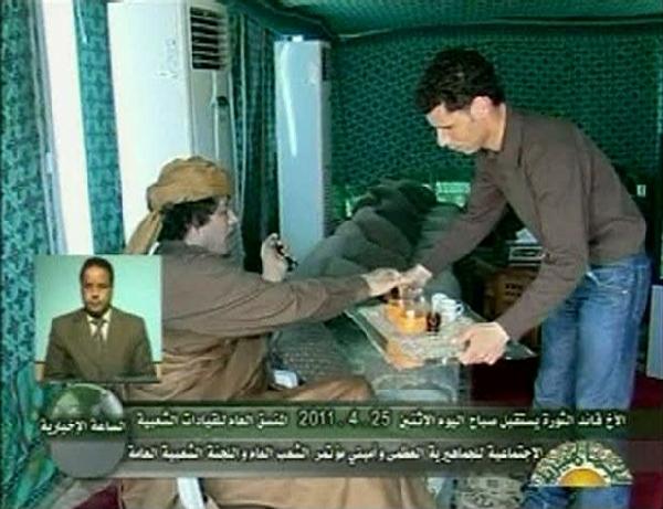 Libyan leader Muammar Gaddafi (L) is served by a man as he meets with leaders of the Social Committee of the People, hours after NATO forces flatten a building inside his Bab al-Aziziyah compound, in a pitched tent in Tripoli in this still image taken from video April 25, 2011. Gaddafi was unhurt in a NATO airstrike on his Bab al-Aziziyah compound early on Monday that left three people dead, a government spokesman said.[Xinhua]