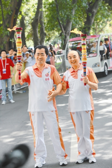 Xuan Zhuxi (L), editor-in-chief of Shenzhen Press Group, with Dan Zhaoyi, a well-known music educator in the Universiade torch relay in Shenzhen University yesterday. Xuan was the 88th runner in the relay and Dan the 87th.Sun Yuchen  