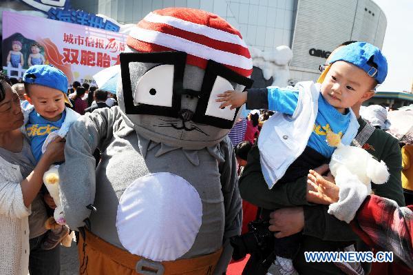 A pair of twins are interested by a cartoon performer during a twins contest in Qingdao, east China's Shandong Province, May 14, 2011. Some 100 pairs of twins participated in the contest at Qingdao Polar Ocean World on Saturday. [Xinhua/Li Ziheng]