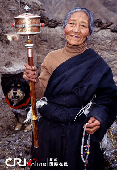 An elderly Tibetan mom rolls a big prayer wheel while taking ritual walk. [Photo/CRI]