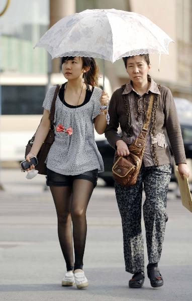 Two pedestrians walk on the street with an umbrella in Yinchuan, capital of northwest China&apos;s Ningxia Hui Autonomous Region, May 17, 2011. Yinchuan was hit by a burning hot weather on Tuesday, with the highest temperature hitting 32 degrees Celsius, marking a record in this year. 