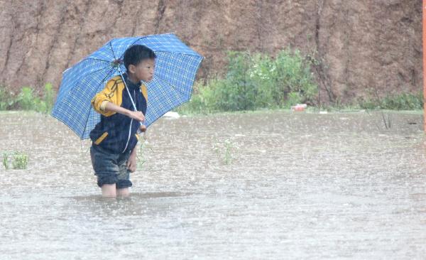 A boy walks in the pool of water on a flooding road after school in Ruichang of Jiujiang City, east China's Jiangxi Province, June 4, 2011. A rainstorm hit most parts of Jiujiang on Saturday. The rainfalls, to last until Monday, will greatly ease the drought the area has suffered for months. [Wei Dongsheng/Xinhua]