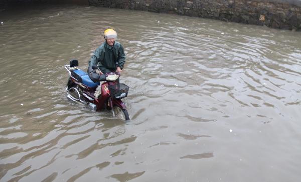 A man walks his motorcycle on a flooding road in Ruichang of Jiujiang City, east China's Jiangxi Province, June 4, 2011. A rainstorm hit most parts of Jiujiang on Saturday. The rainfalls, to last until Monday, will greatly ease the drought the area has suffered for months. [Wei Dongsheng/Xinhua]