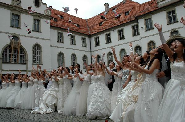 Chinese bridal couples taking part in a collective wedding event throw flowers into the air at New Swan Stone Castle in Fuessen, south Germany, on June 3, 2011. A total of 31 couples from north China's Tianjin Municipality held a collective wedding on Friday at New Swan Stone Castle, one of the most popular travel destinations in Europe. [Xinhua/Wu Mei]