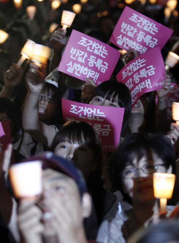 University students holding candles and signs shout slogans during a rally demanding tuition fees cuts in central Seoul, June 7, 2011. [China Daily/Agencies]