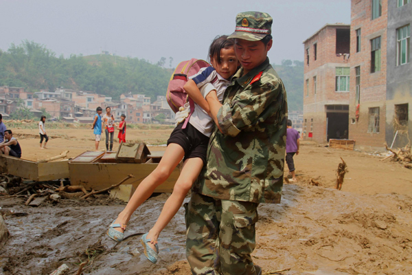 A soldier helps a girl across the muddy road in Wangmo County in Guizhou Province on June 8. Rainstorms-triggered flood has caused heavy casualties and property losses in the area since June 5. 