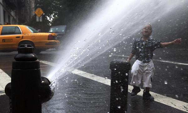 A child plays under the spray of a fire hydrant in Riverside, Manhattan on a day that temperatures soared in New York June 9, 2011. [China Daily/Agencies]