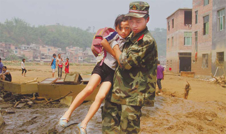 A soldier with the People's Armed Police helps a girl across a muddy field on Wednesday in Wangmo, Guizhou province, after floods ravaged the county on Sunday and Monday.
