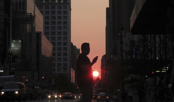 A pedestrian checks his phone while crossing 34th Street in Manhattan as the sun sets on New York, June 8, 2011.