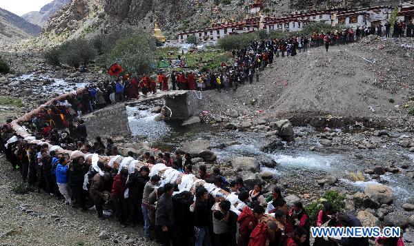 People carry the Buddha Tangka painting out of Curpu Temple, 70 kilometers away from Lhasa, capital of southwest China&apos;s Tibet Autonomous Region, June 12, 2011. The annual Buddha Tangka painting unfolding ceremony was held in Curpu Temple on Sunday. [Xinhua]