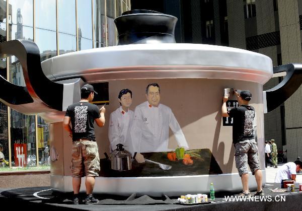 Two workers panit a gaint pot model with 4-meter diameter in front a mall in Shenyang, capital of northeast China&apos;s Liaoning Province, June 13, 2011. [Xinhua]