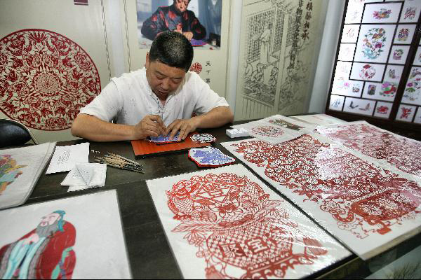 Tian Dianliang, successor of Weixian County paper cutting, makes paper-cut works in an exhibition of Chinese classics and intangible culture heritages in the National Library of China in Beijing, capital of China, June 8, 2011. The exhibition showcases about 200 historical documents about China's intangible heritages and many heritage successors are invited to show their skills on the spot. [Photo/Xinhua/Zhao Bing]