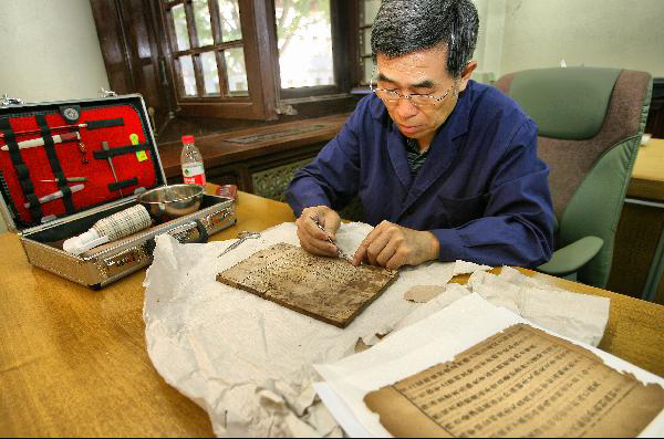 A staff member of the National Library of China restores ancient classic books in an exhibition of Chinese classics and intangible culture heritages in the National Library of China in Beijing, capital of China, June 8, 2011. The exhibition showcases about 200 historical documents about China's intangible heritages and many heritage successors are invited to show their skills on the spot. [Photo/Xinhua/Zhao Bing]