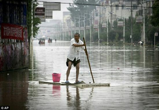 Devastating: A man rows through a flooded street in Xianing, Hubei province, using a makeshift raft. [CNTV]