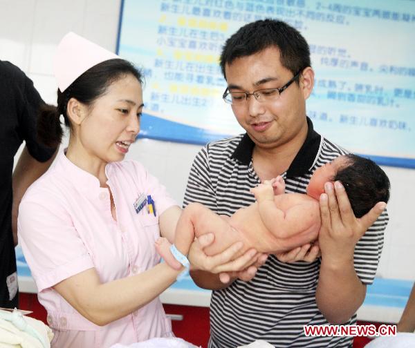 A freshmen father holds his baby under the nurse's instruction in the No. 1 People's Hospital in Xiangyang, central China's Hubei Province, June 18, 2011. [Xinhua/Gong Bo] 