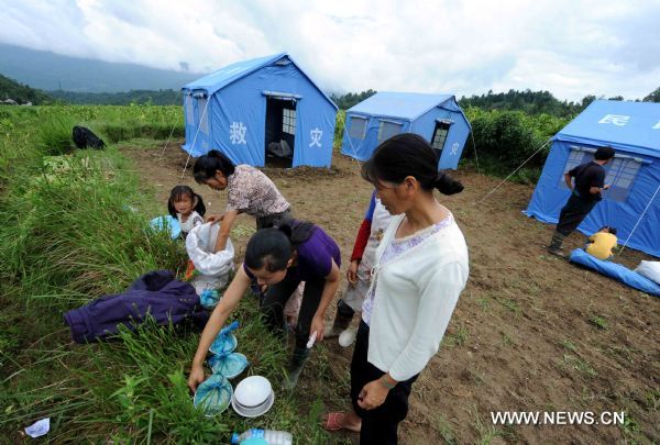 Displaced people have a meal next to makeshift tents after an earthquake in Tengchong County, southwest China's Yunnan Province, June 21, 2011. The 5.2-magnitude earthquake that hit Tengchong on Monday has left six people injured and caused significant economic losses, the Ministry of Civil Affairs said Tuesday. As of 3 p.m. Tuesday, the quake had affected 22,000 local residents and led to the emergency relocation of 2,168 people. The local government has allocated 7 million yuan to set up a disaster relief fund, as well as sent hundreds of tents, quilts and articles of clothing to the quake zone, according to the ministry. (Xinhua/Yang Zongyou) (hdt) 