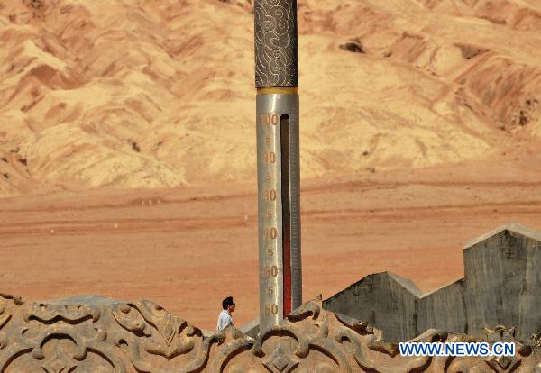 A tourist passes by a large thermometer displaying temperature of nearly 72 degrees Celsius in the Flaming Mountain scenic area of Turpan, a basined area of northwest China's Xinjiang Uygur Autonomous Region, June 22, 2011. [Xinhua/Jiang Xiaoming] 